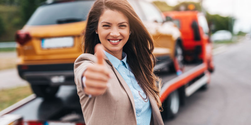 smiling woman gives thumbs up as her car is towed away