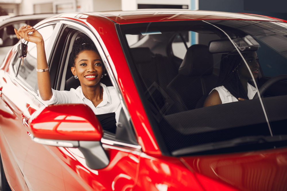 woman in car color red holds key new car owner